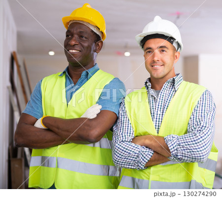 Portrait of two positive engineers in yellow vest and safety helmet in renovated cottage 130274290