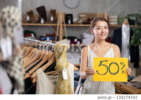 Girl with poster in hands announces discounts 50 percent in womens clothing store. Girl with poster in hands announces discounts 50 percent in womens clothing store. 130274502