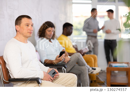 Middle-aged male visitor sitting on chair in waiting hall of clinic Middle-aged male visitor sitting on chair in waiting hall of clinic 130274557