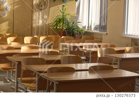 A bright and airy classroom filled with rows of wooden desks and chairs, ready for a lesson. 130276373