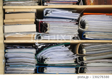 Stacks of files, binders, and documents on wooden shelves inside a cabinet. 130276380
