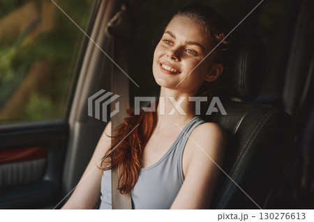 Smiling young woman with long hair in sporty attire, enjoying a sunny drive in a car, exuding happiness and relaxation, with a soft green background Smiling young woman with long hair in sporty attire, enjoying a sunny drive in a car, exuding happiness and relaxation, with a soft green background 130276613