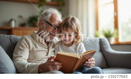 Grandfather reading a book to his grandchild in a bright living room, both smiling. Grandfather reading a book to his grandchild in a bright living room, both smiling. 130277685
