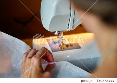 Person sewing fabric on electric sewing machine at home Person sewing fabric on electric sewing machine at home 130278333