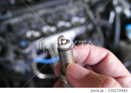 Close up of a worn spark plug held by hand with blurred engine in background Close up of a worn spark plug held by hand with blurred engine in background 130278482