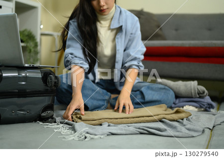 Young woman folding clothes on floor while packing suitcase for travel at home Young woman folding clothes on floor while packing suitcase for travel at home 130279540