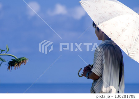 ＜素材＞夏の海と向日葵を眺める日傘の女性 130281709