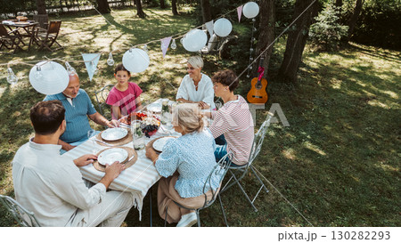 Areal view of grandparents, parents and kids dining together outside. Areal view of grandparents, parents and kids dining together outside. 130282293