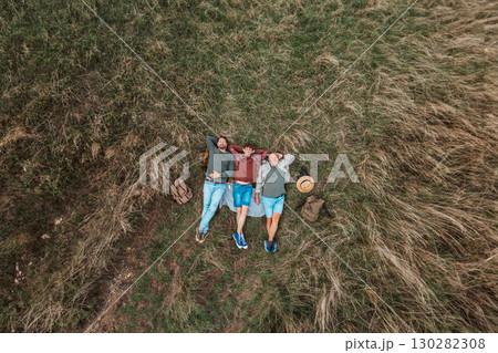 Areal view of grandfather, father and teen boy lying in grass and resting during hiking trip. Areal view of grandfather, father and teen boy lying in grass and resting during hiking trip. 130282308