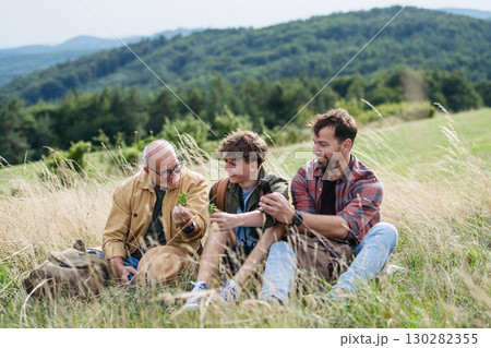 Grandfather, father and teen boy hiking togeter in nature, resting on meadow. 130282355