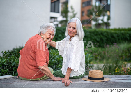 Elderly mother sitting on bench with adult daughter 130282362