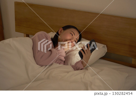 布団の中でスマホを使う女性　眠気 130282454