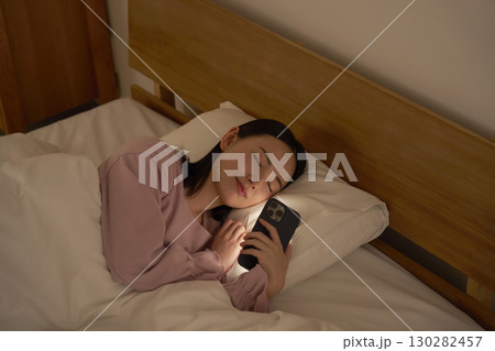 布団の中でスマホを使いながら寝落ちする女性 布団の中でスマホを使いながら寝落ちする女性 130282457