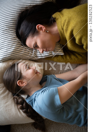 Top view of girl and mom talking in bed, lying face to face. Top view of girl and mom talking in bed, lying face to face. 130282523