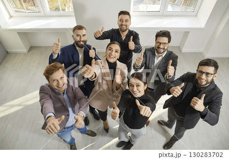 Team of happy, smiling business men and women standing in office, looking up and showing thumbs up 130283702