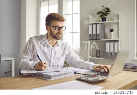Young business man working at the desk with a pile of documents on his workplace at office. Young business man working at the desk with a pile of documents on his workplace at office. 130283739