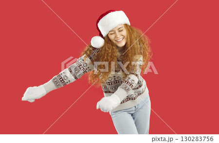 Funny dancing playful redhead girl in Christmas Santa hat, mittens and sweater on red background. Funny dancing playful redhead girl in Christmas Santa hat, mittens and sweater on red background. 130283756