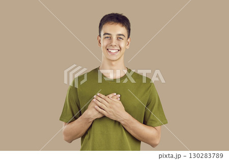 Portrait of touched positive teenage guy holding hands on chest expressing gratitude. Portrait of touched positive teenage guy holding hands on chest expressing gratitude. 130283789