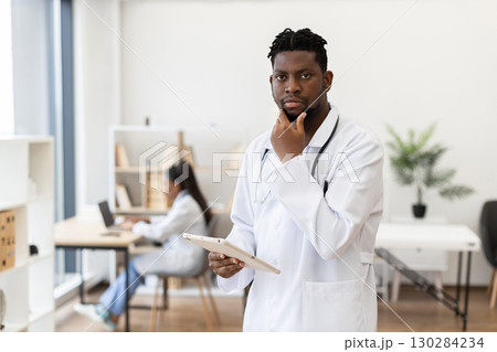 Male adult doctor with tablet posing in a bright clinic interior, professional attire Male adult doctor with tablet posing in a bright clinic interior, professional attire 130284234