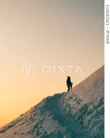 Silhouette of young person climbing snow covered mountain during beautiful sunset, conveying sense of adventure, challenge, and achievement. Mountaineer, snow covered peak, golden sunset 130284611
