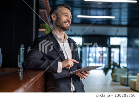 Caucasian man at the reception standing with a tablet in hands and looking confident Caucasian man at the reception standing with a tablet in hands and looking confident 130285550