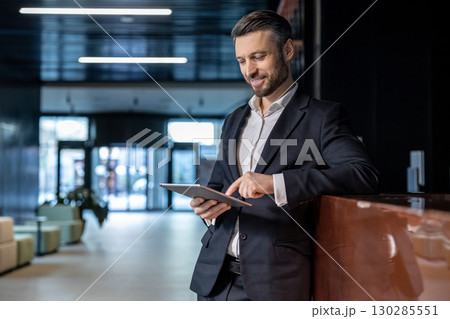Caucasian man at the reception standing with a tablet in hands and looking confident Caucasian man at the reception standing with a tablet in hands and looking confident 130285551
