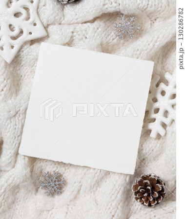 Square blank card on white knitted sweater near Christmas decor, winter Holiday mockup 130286782