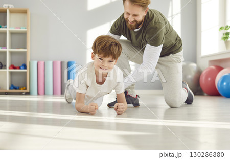 Dad trains his preteen son in bright gym and teaches him to stand in plank position. 130286880