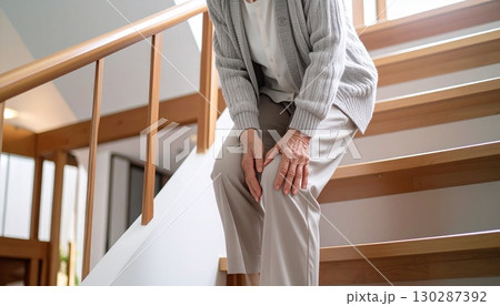 膝をさすりながらゆっくりと慎重に階段を降りる高齢者 膝の痛みとシニアライフのイメージ 膝をさすりながらゆっくりと慎重に階段を降りる高齢者 膝の痛みとシニアライフのイメージ 130287392