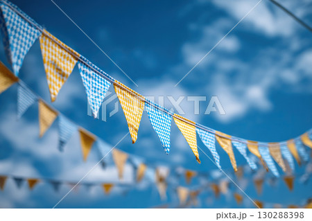 A garland of blue and yellow triangular flags or bunting fluttering diagonally against a clear blue sky. Symbolizes celebration, fun, and outdoor activities. 130288398