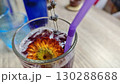 A glass of purple iced lemonade decorated with a vibrant edible flower and lavender sprigs. The image evokes freshness, creativity and botanical-inspired summer drinks 130288688