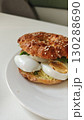 Bagel sandwich with sesame topping filled with sliced boiled egg, avocado and greens on a white plate. The image represents a healthy breakfast or brunch with simple ingredients 130288690