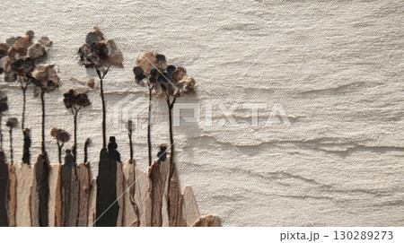Dried flower arrangement with tall stems and textured petals on beige fabric background creating natural and rustic atmosphere 130289273