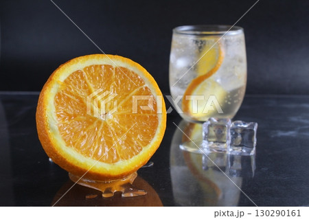 lemonade with orange and ice in a glass on a black background next to lies ice and orange. Summer drink on a black background 130290161
