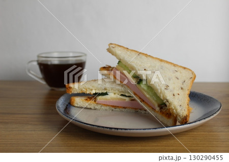 Breakfast snack lunch sandwich with sausage ham cheese cucumber lies on a plate next to a cup of tea or coffee. Morning serve. preparation. Cafe Restaurant Breakfast snack lunch sandwich with sausage ham cheese cucumber lies on a plate next to a cup of tea or coffee. Morning serve. preparation. Cafe Restaurant 130290455