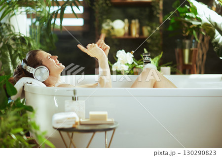 Joyful Woman Enjoying Music in a Lush Bubble Bath Joyful Woman Enjoying Music in a Lush Bubble Bath 130290823