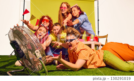 Group of friends reaching hands toward fan with playful smiles on green background Group of friends reaching hands toward fan with playful smiles on green background 130291019