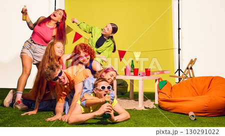 Pile of young friends stacked on grass with drinks and party smiles 130291022