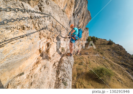 Climber on via ferrata trail, crossing a steep mountain edge 130291946