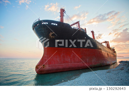 Red cargo ship stranded in a shallow sea under sunset sky with clouds Red cargo ship stranded in a shallow sea under sunset sky with clouds 130292643