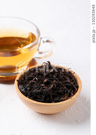 Dried black tea leaves in wooden bowl and hot tea in cup glass  130293648