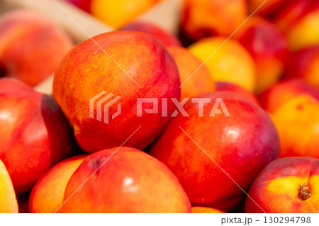 Close-up a lot of fresh red yellow colored peaches on market stall or in groceries shop area. Nectarines background. Fruit food background. Selective focus Close-up a lot of fresh red yellow colored peaches on market stall or in groceries shop area. Nectarines background. Fruit food background. Selective focus 130294798