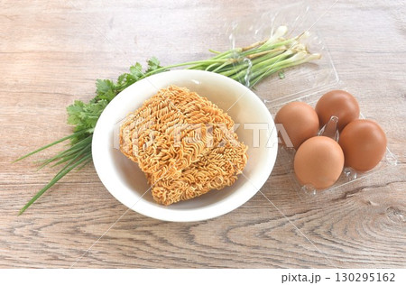 dry instant noodles on bowl with raw egg in plastic packaging and spring onion couple parsley prepare to cooking 130295162