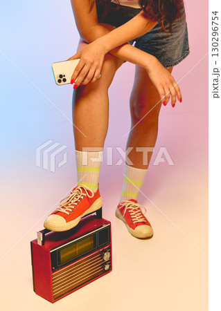 Woman holding smartphone with retro red radio on pastel background Woman holding smartphone with retro red radio on pastel background 130296754