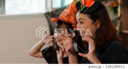 Halloween celebration with mother and daughter wearing spooky hats and playful expressions Halloween celebration with mother and daughter wearing spooky hats and playful expressions 130296911