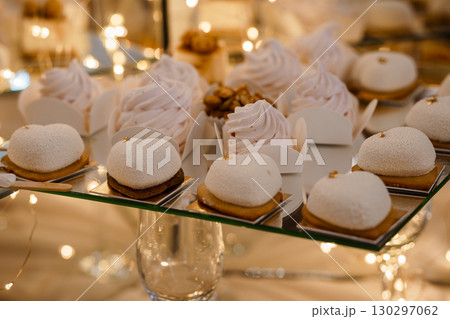 Elegant Dessert Display with White Chocolate Cream Puffs and Miniature Cakes on Tiered Stand, Blurred Golden Lights. 130297062