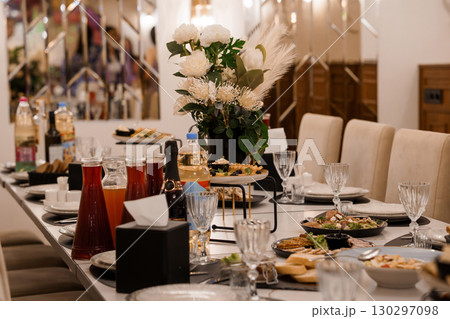Elegant Dinner Party Setup with White Floral Arrangement, Drinks, Appetizers, and Table Setting in a Modern Interior. 130297098