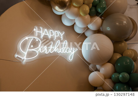 Modern Beige Balloon Garland Backdrop with Neon "Happy Birthday" Sign for Celebration and Party Decor, Warm Toned Event Setup 130297148