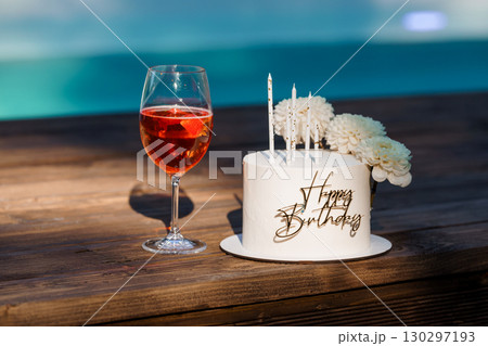 Celebratory Birthday Scene with Rose Wine, Cake and Candles by a Swimming Pool, Warm Lighting and Wooden Texture. 130297193