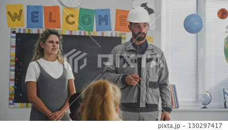 Construction Worker in Uniform Speaking to Curious Students About Work on Construction Site 130297417